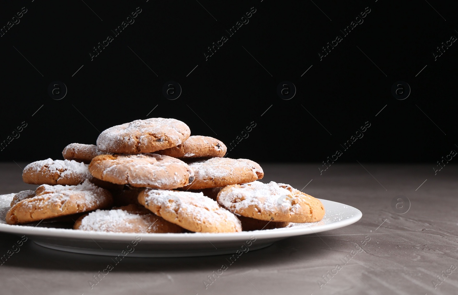 Photo of Woman with sieve sprinkling powdered sugar onto cookies at grey textured table, closeup