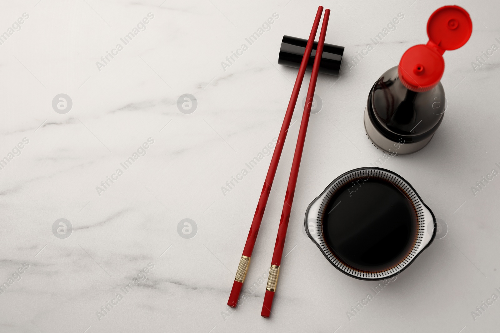 Photo of Bowl, bottle with soy sauce and chopsticks on white marble table, flat lay. Space for text