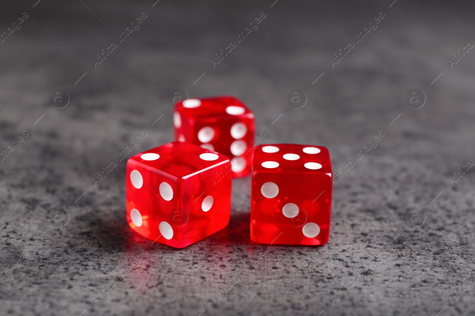 Photo of Three red game dices on grey textured table, closeup