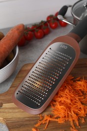 Photo of Hand grater and fresh ripe carrot on wooden board, closeup