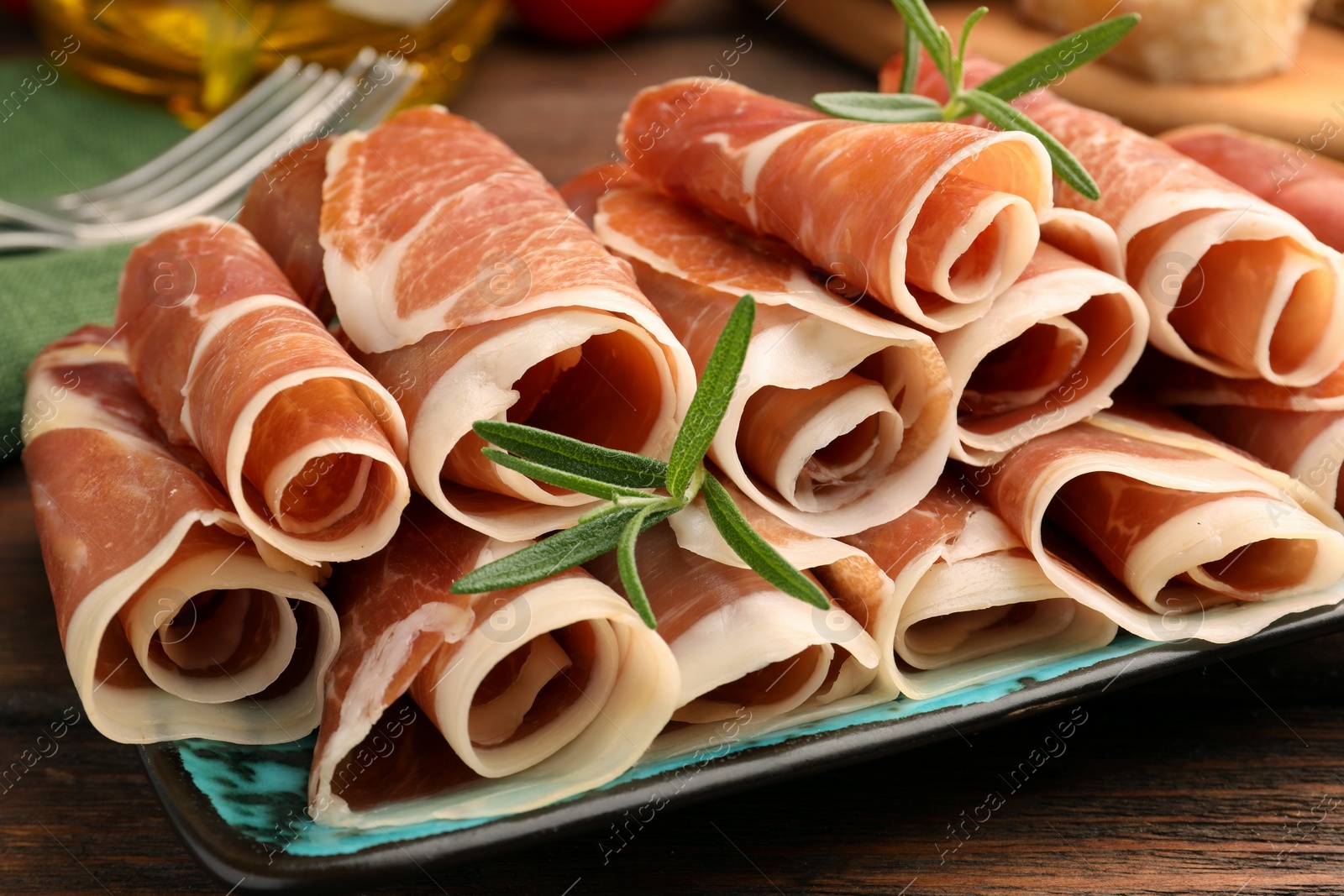 Photo of Rolled slices of delicious jamon with rosemary on table, closeup