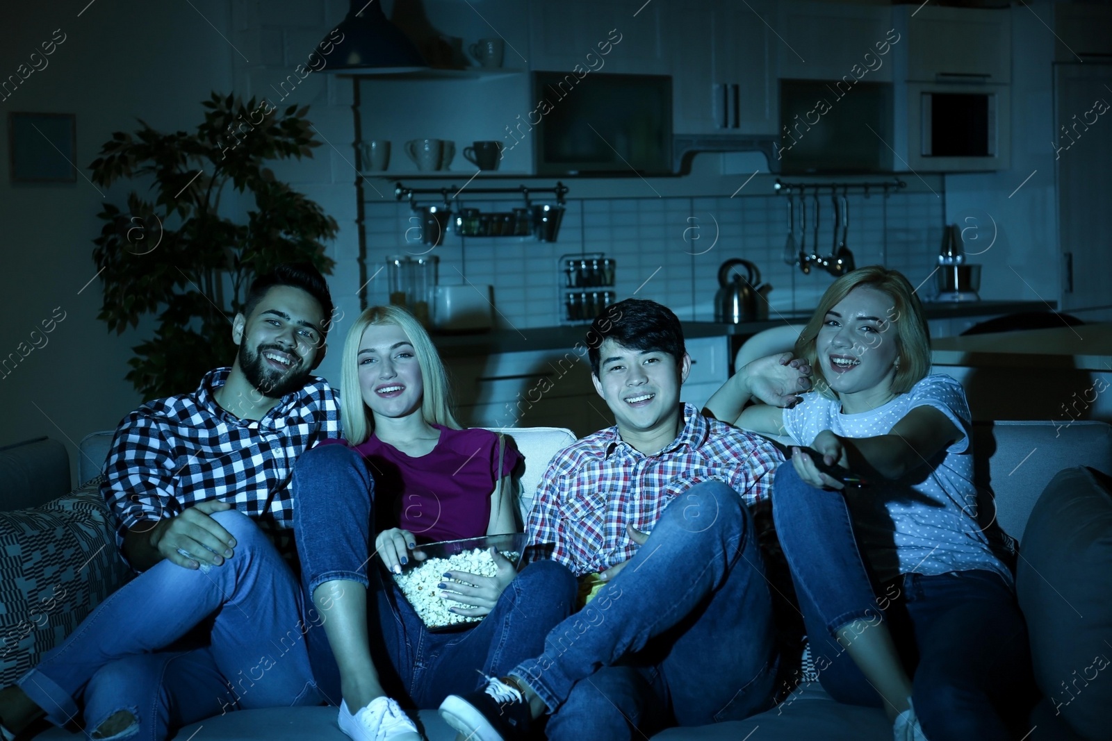 Photo of Young friends with snacks watching TV on sofa at night