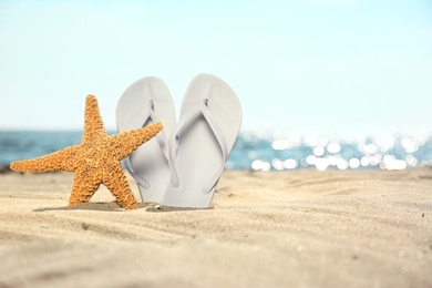 Photo of Starfish and flip flops on sand near sea, space for text. Beach objects