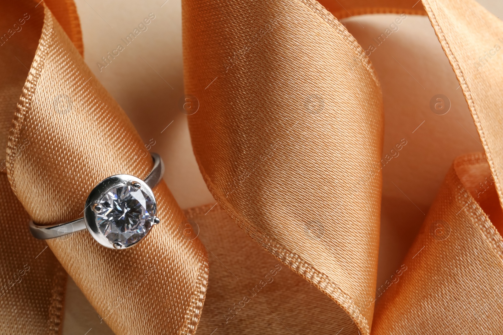 Photo of Beautiful luxury engagement ring with gemstone and ribbon on beige background, closeup