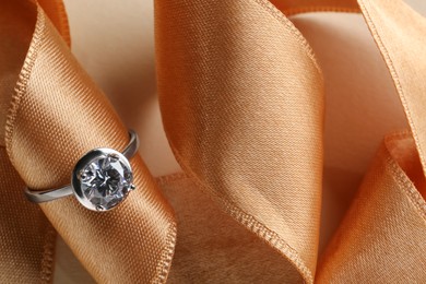 Beautiful luxury engagement ring with gemstone and ribbon on beige background, closeup