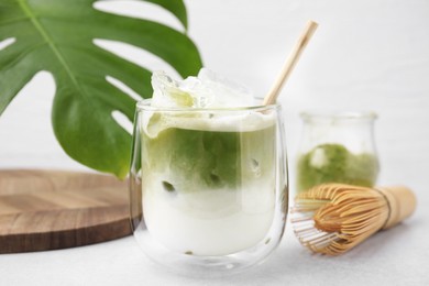 Photo of Glass of tasty iced matcha latte, leaf and bamboo whisk on white table, closeup