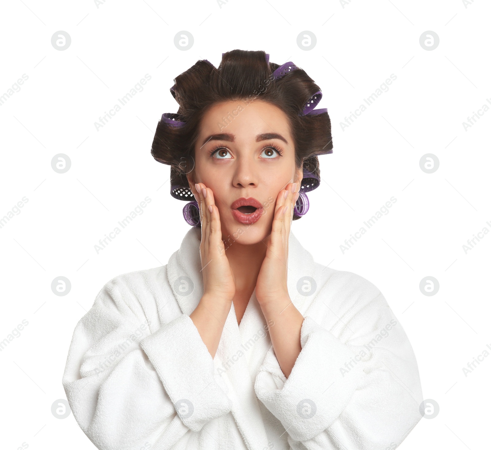 Photo of Emotional young woman in bathrobe with hair curlers on white background