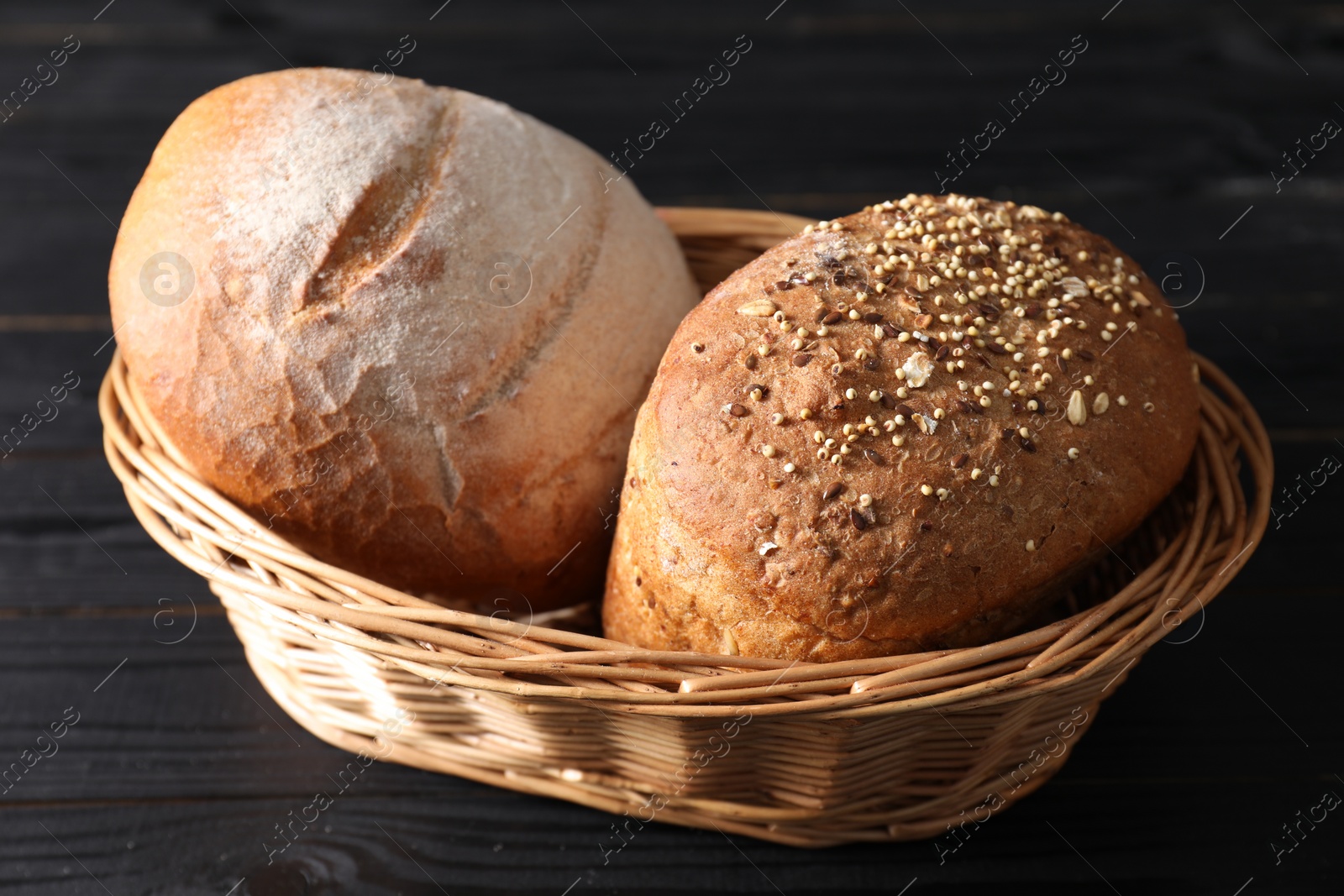 Photo of Wicker basket with fresh bread on black wooden table
