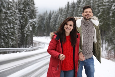 Couple walking near snowy forest, space for text. Winter vacation