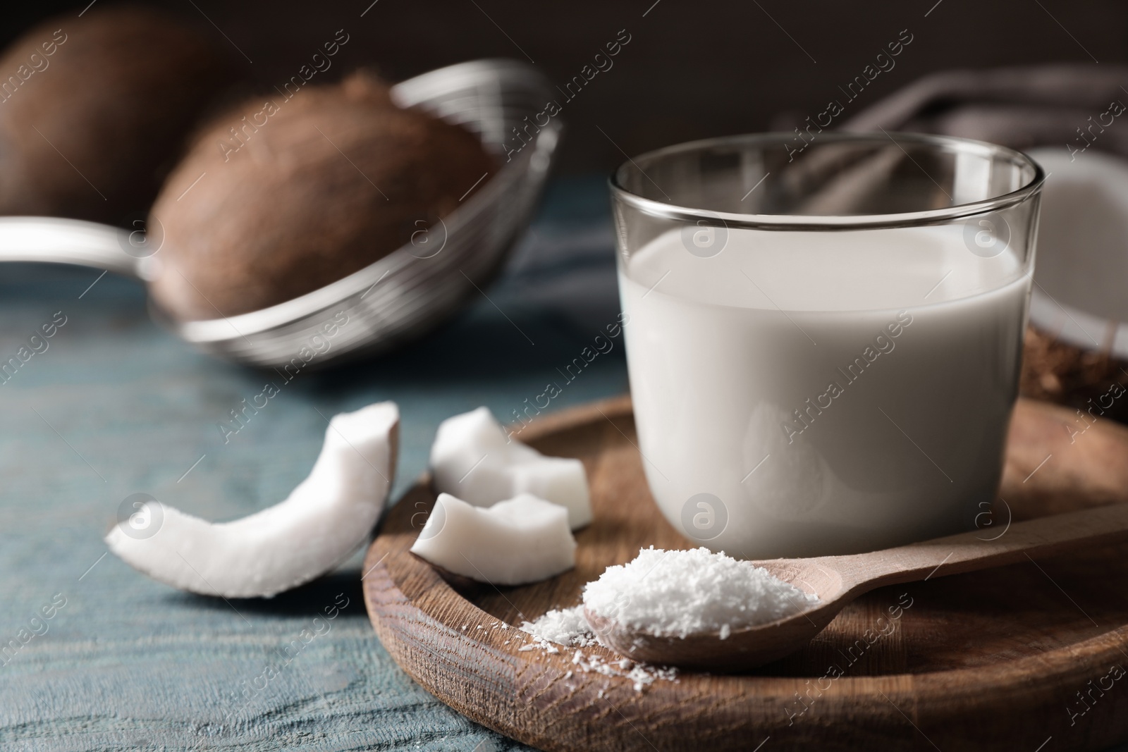 Photo of Glass of delicious coconut milk, spoon with flakes and nuts on wooden table, closeup. Space for text