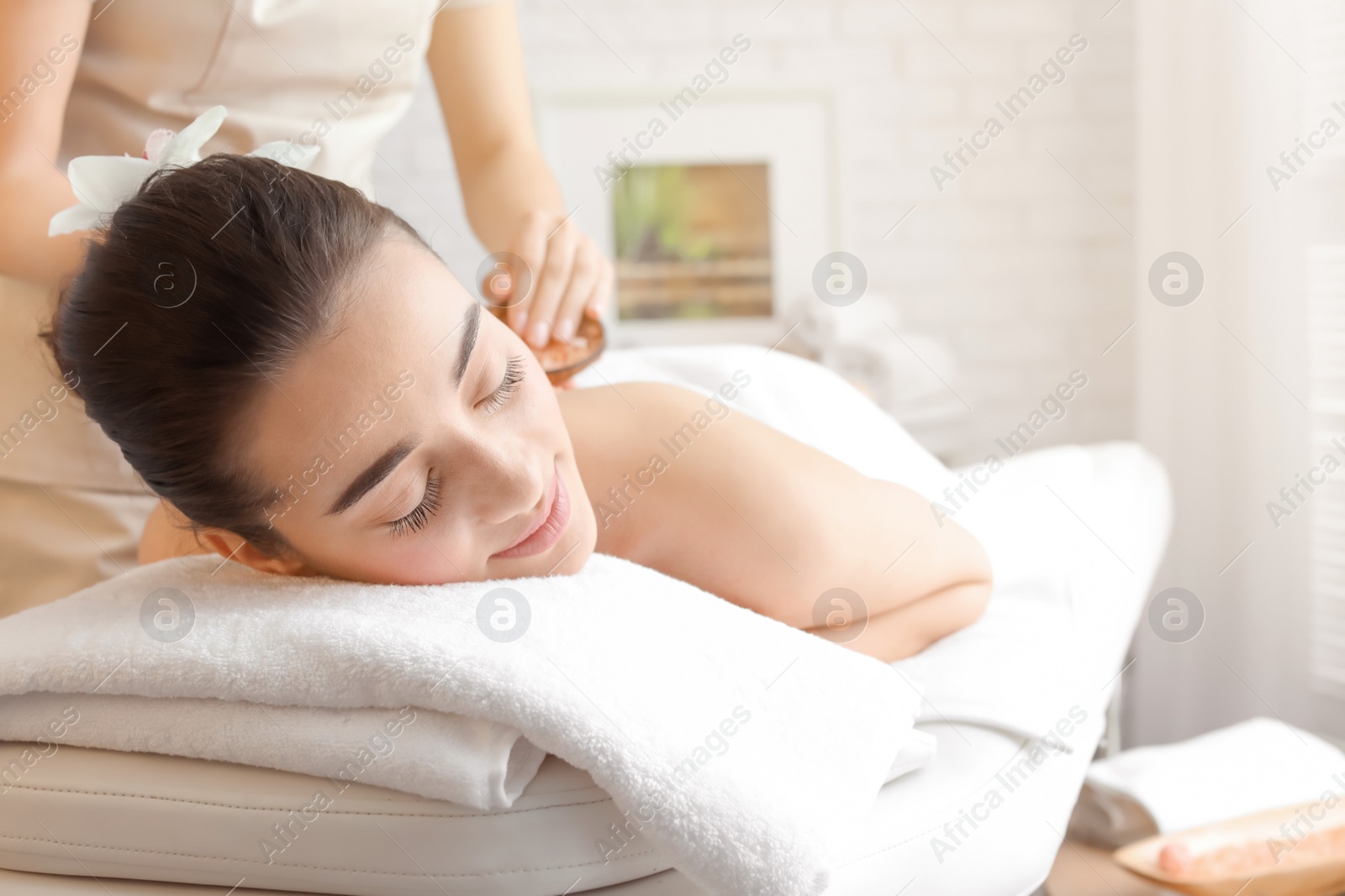 Photo of Young woman having body scrubbing procedure with sea salt in spa salon