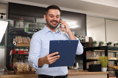 Photo of Business owner with clipboard talking on phone in his cafe