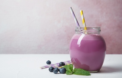 Jar of tasty milk shake and blueberries on table. Space for text