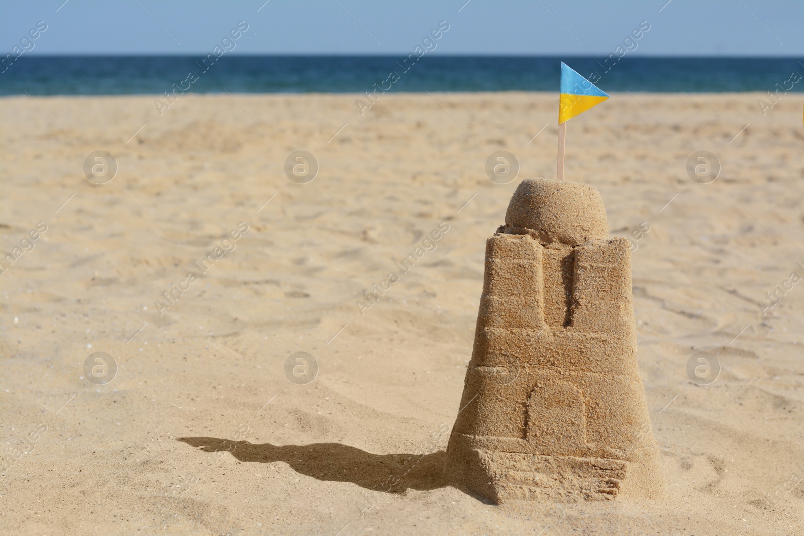 Photo of Beautiful sand castle with small Ukrainian flag on beach near sea, space for text