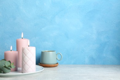 Scented candles, eucalyptus and cup on grey table near light blue wall, space for text
