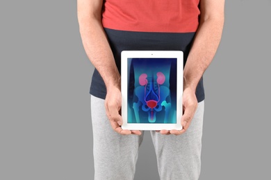 Photo of Mature man holding tablet with urinary system on screen against grey background