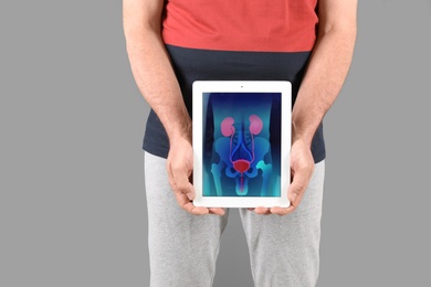 Mature man holding tablet with urinary system on screen against grey background