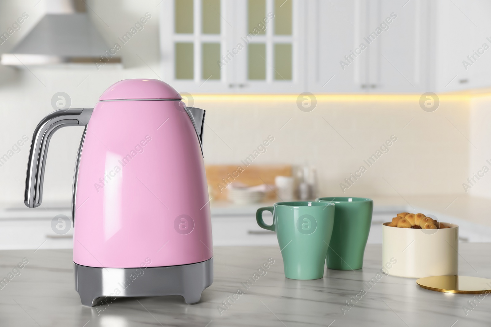 Photo of Modern electric kettle, cups and cookies on table in kitchen