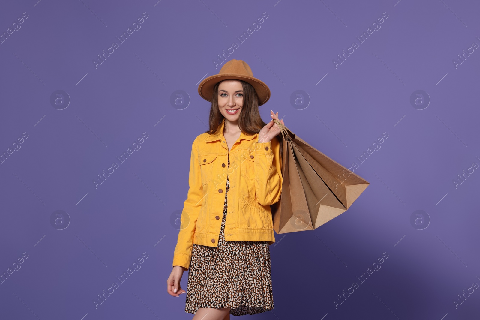 Photo of Stylish young woman with shopping bags on purple background