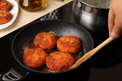 Photo of Woman cooking vegan cutlets in frying pan on cooktop, closeup
