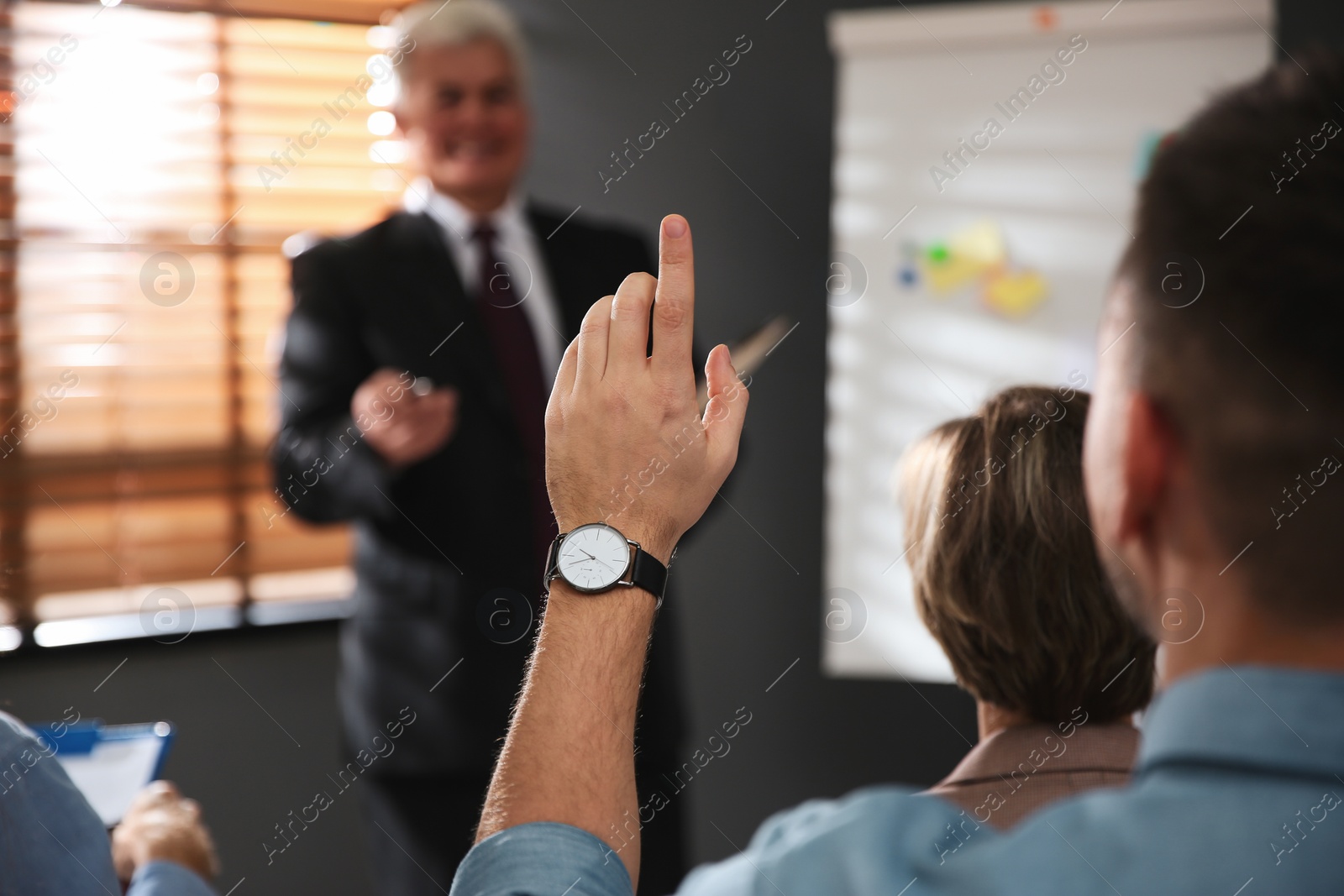 Photo of Man raising hand to ask question at seminar in office