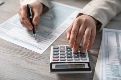 Payroll. Woman using calculator while working with tax return forms at wooden table, selective focus