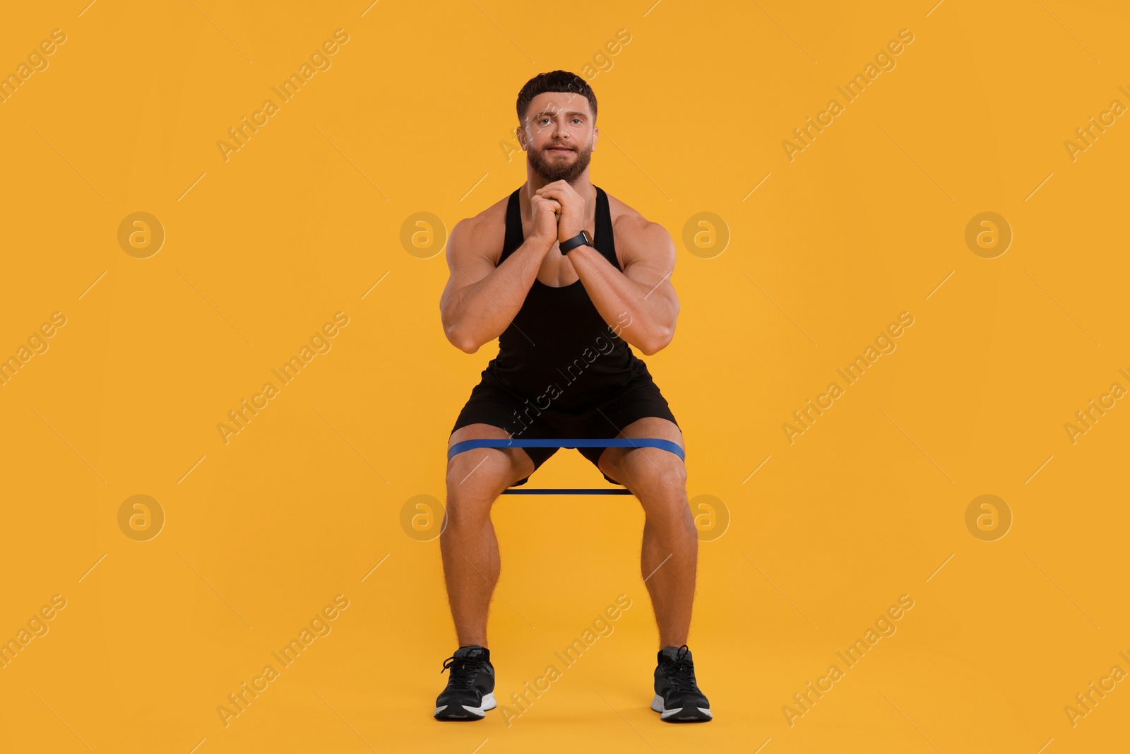 Photo of Young man exercising with elastic resistance band on orange background