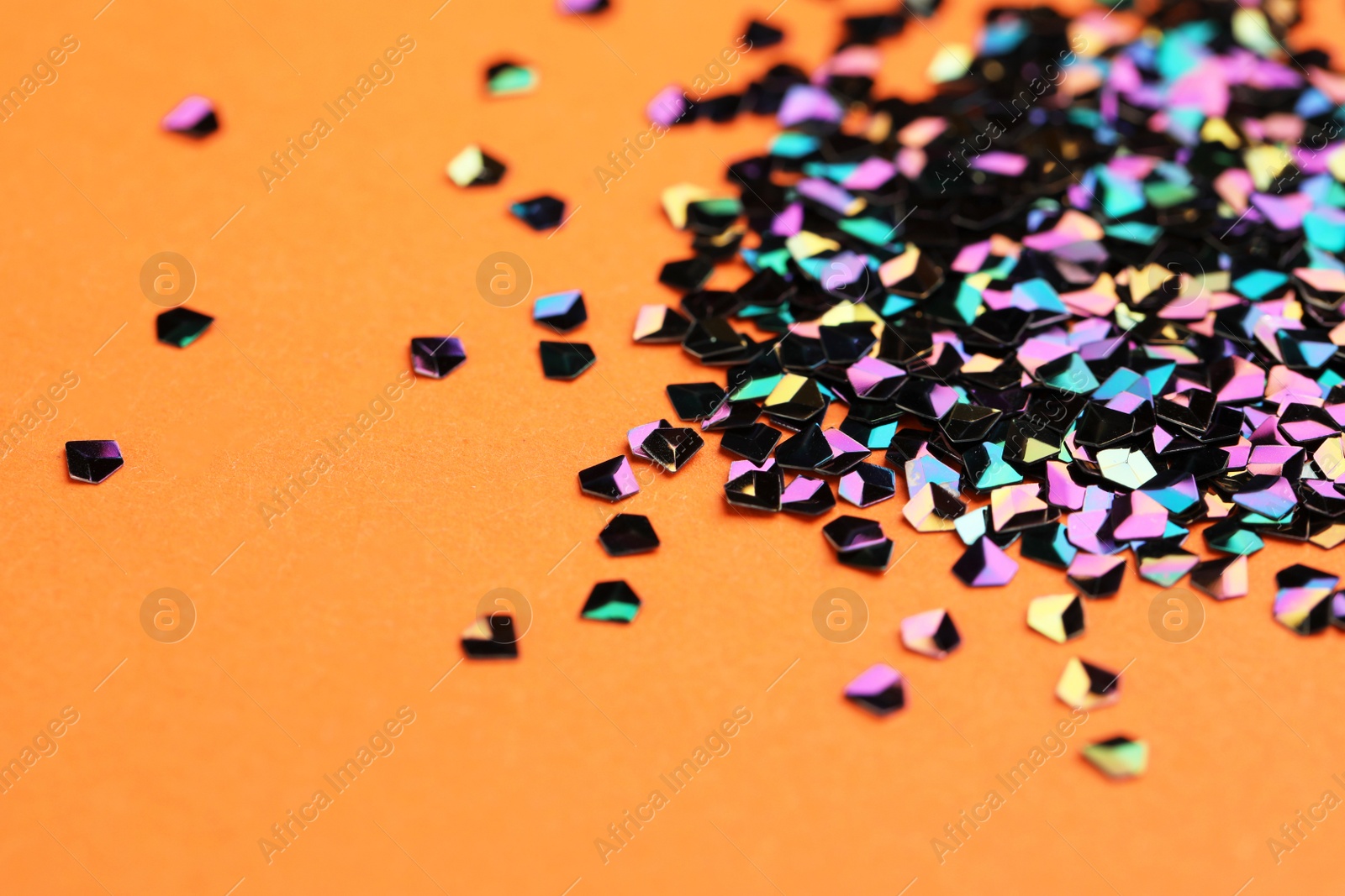 Photo of Pile of shiny glitter on orange background, closeup