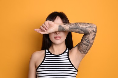 Photo of Beautiful woman with tattoos on arm against yellow background