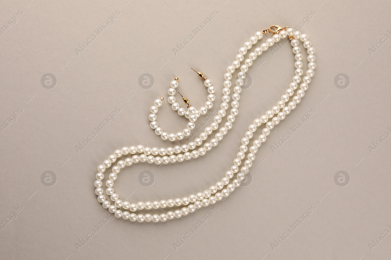 Photo of Elegant pearl necklace and earrings on beige background, top view