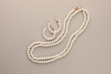 Photo of Elegant pearl necklace and earrings on beige background, top view