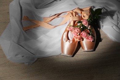 Photo of Ballet shoes. Elegant pointes and bouquet of roses on wooden floor, space for text