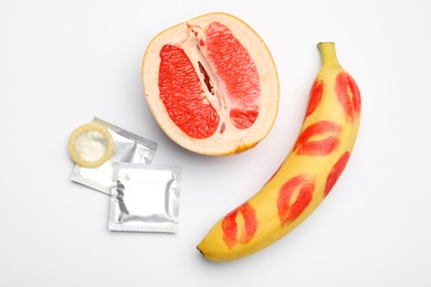 Photo of Condoms, cut grapefruit and banana with lipstick kiss marks on white background, flat lay. Safe sex