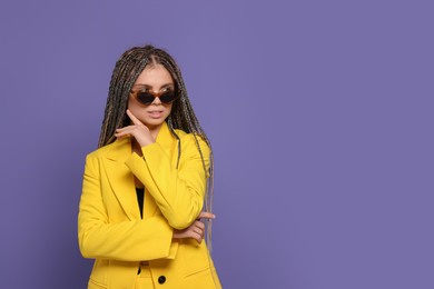 Beautiful woman with long african braids and sunglasses on purple background, space for text
