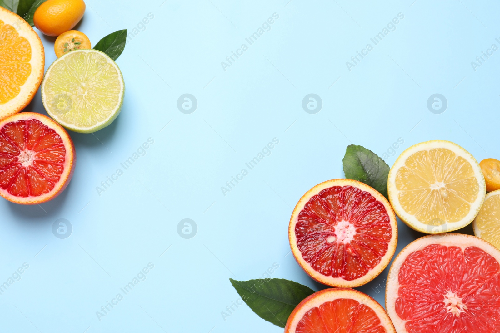 Photo of Fresh juicy citrus fruits with green leaves on light blue background, flat lay. Space for text