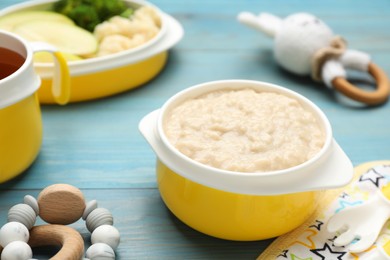 Photo of Toys and plastic dishware with healthy baby food on light blue wooden table, closeup