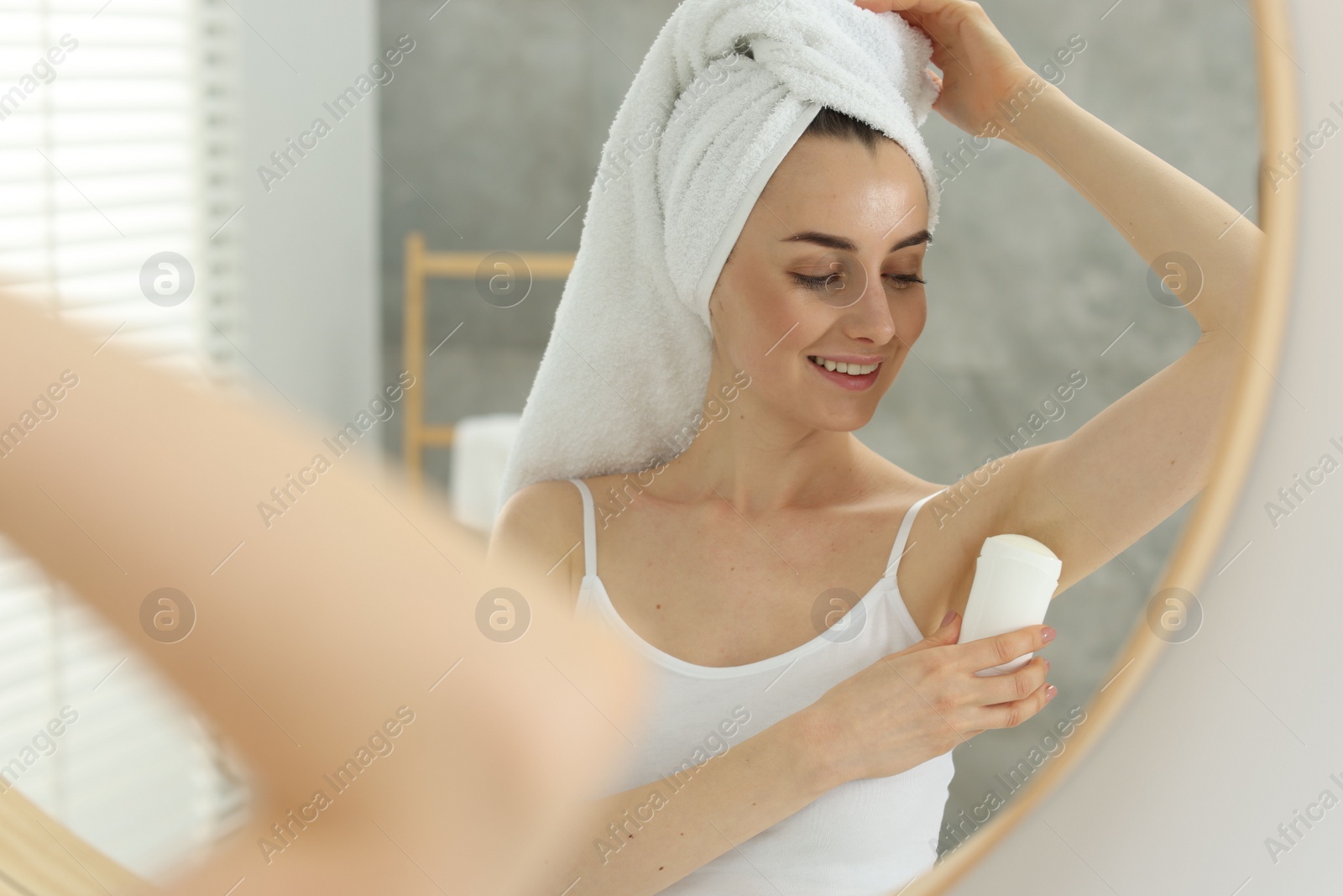 Photo of Beautiful woman applying deodorant near mirror in bathroom