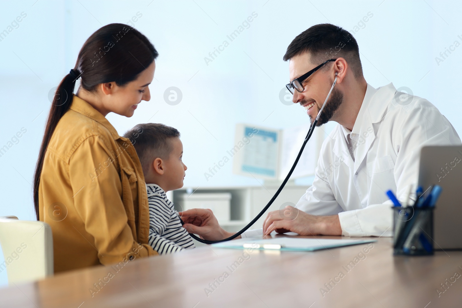 Photo of Mother and son visiting pediatrician in hospital. Doctor examining little boy