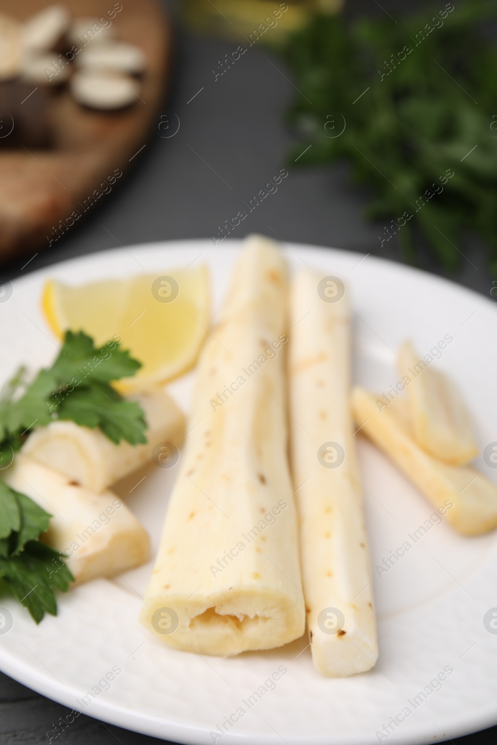 Photo of Cut raw salsify roots with parsley and lemon on white plate, closeup