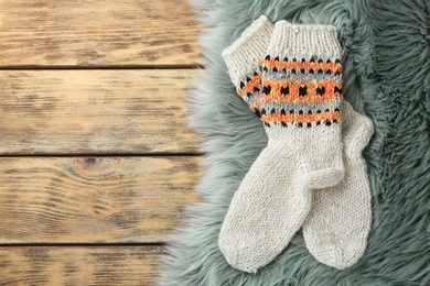 Photo of Knitted socks and grey faux fur on wooden table, flat lay. Space for text