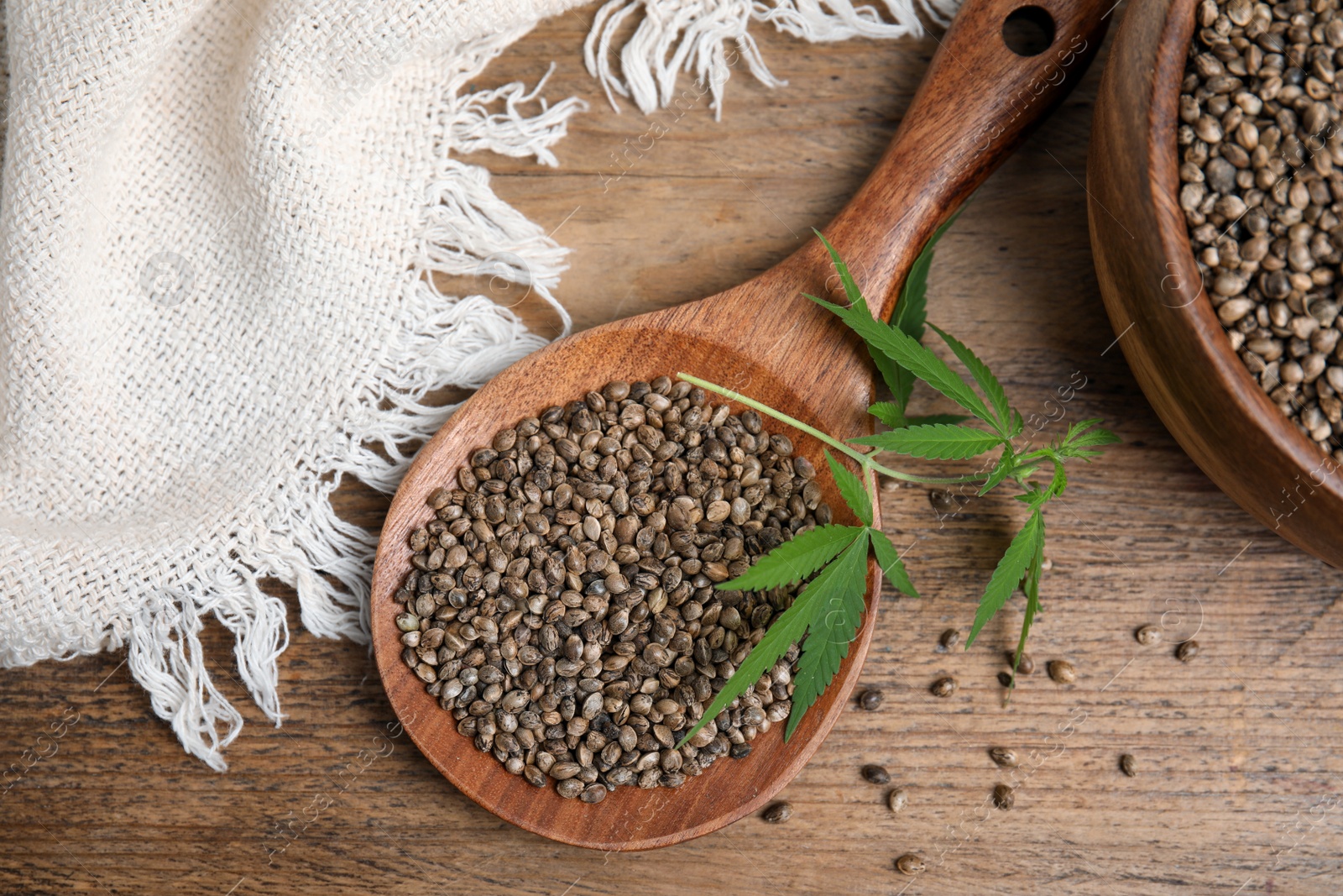 Photo of Organic hemp seeds and leaves on wooden table, flat lay