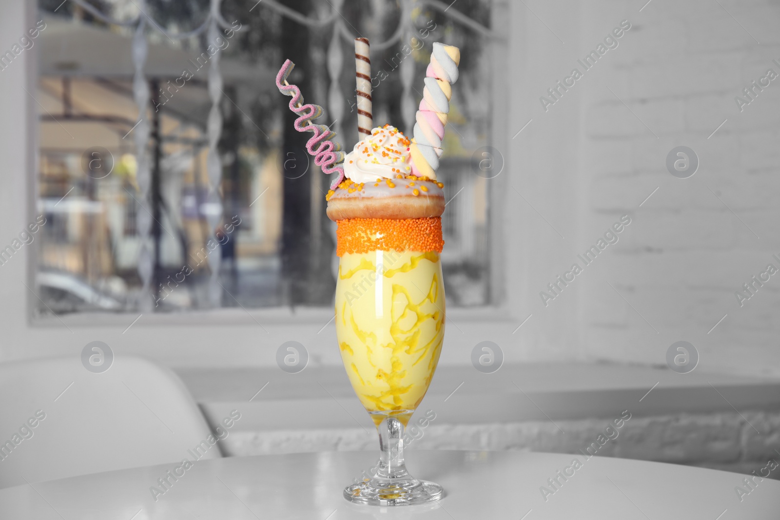 Photo of Glass of tasty milk shake with sweets on table indoors