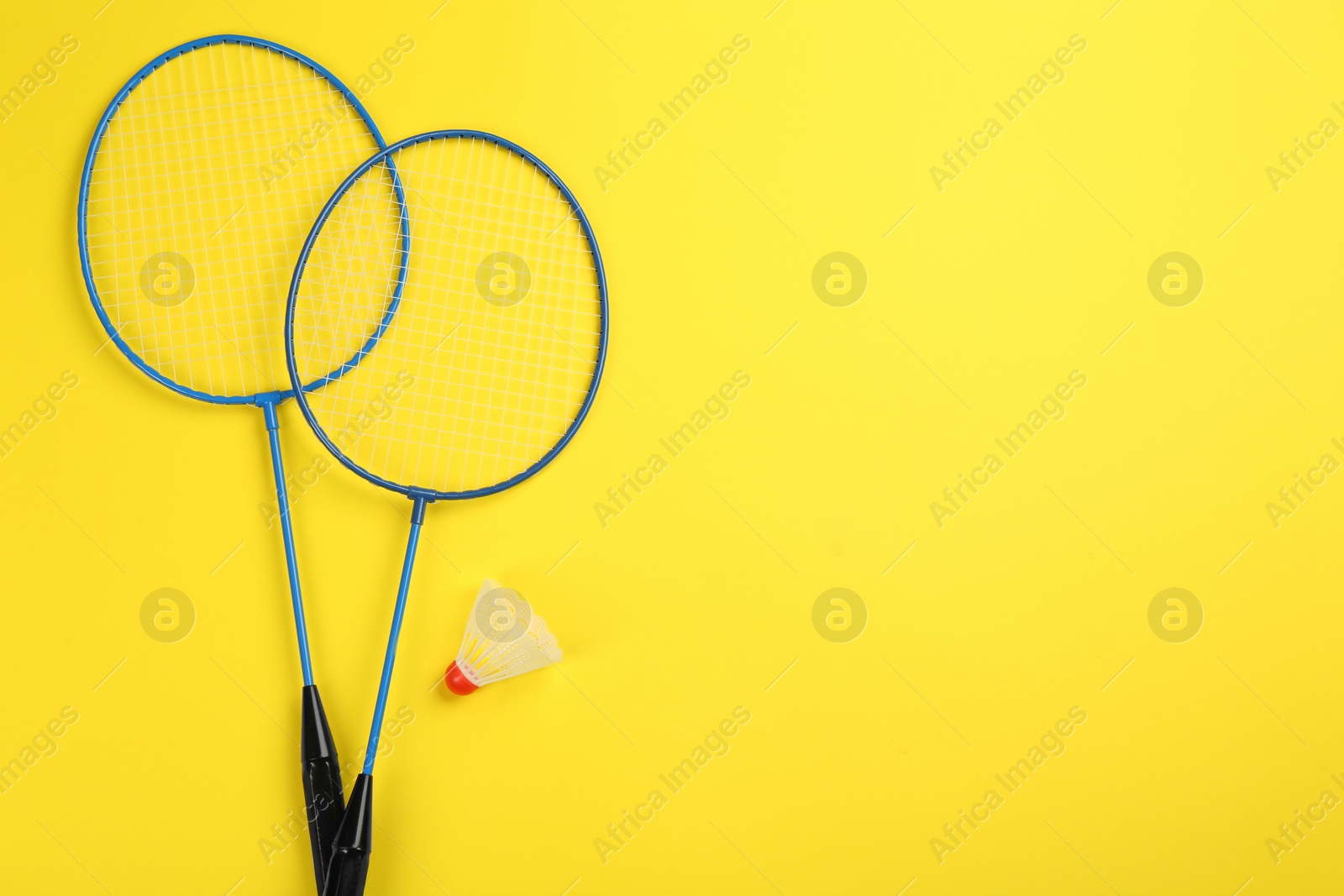 Photo of Rackets and shuttlecock on yellow background, flat lay with space for text. Badminton equipment