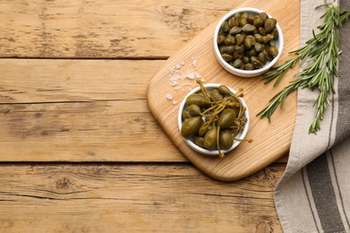 Photo of Delicious pickled capers and rosemary twigs on wooden table, top view. Space for text