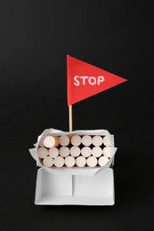 Photo of Cigarettes in pack and red flag with word Stop on black background. Quitting smoking concept