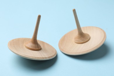 Photo of Two wooden spinning tops on light blue background, closeup