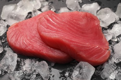 Raw tuna fillets and ice cubes on dark table