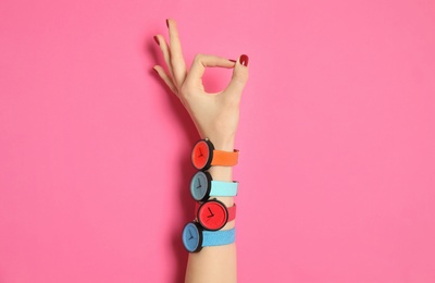 Woman with many bright wrist watches on color background, closeup. Fashion accessory