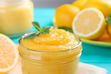 Photo of Delicious lemon curd in glass jar and mint on light blue table, closeup