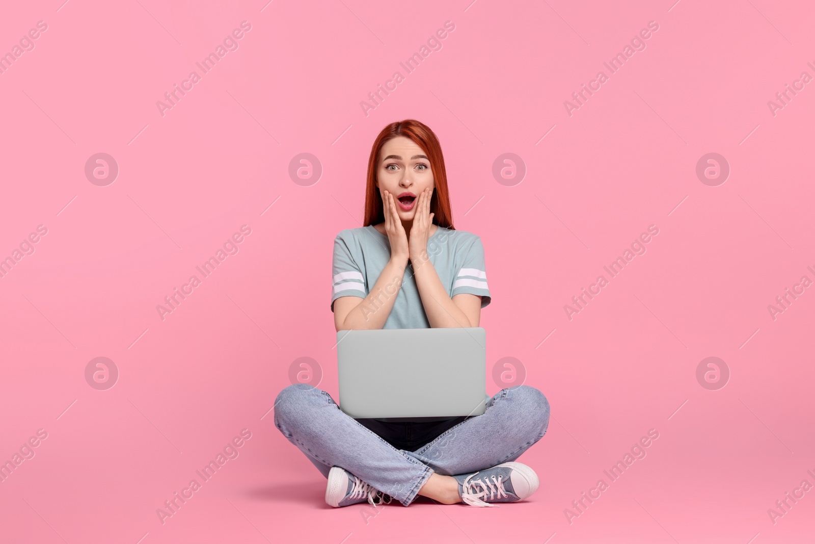 Photo of Surprised young woman with laptop on pink background